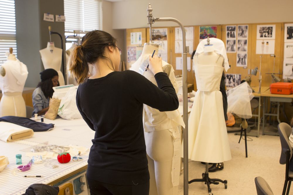 Two Student sone sitting and the other designing on a mannequin