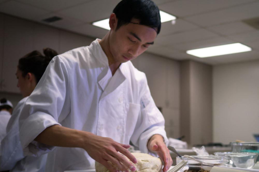 A student kneading a dough in food lab